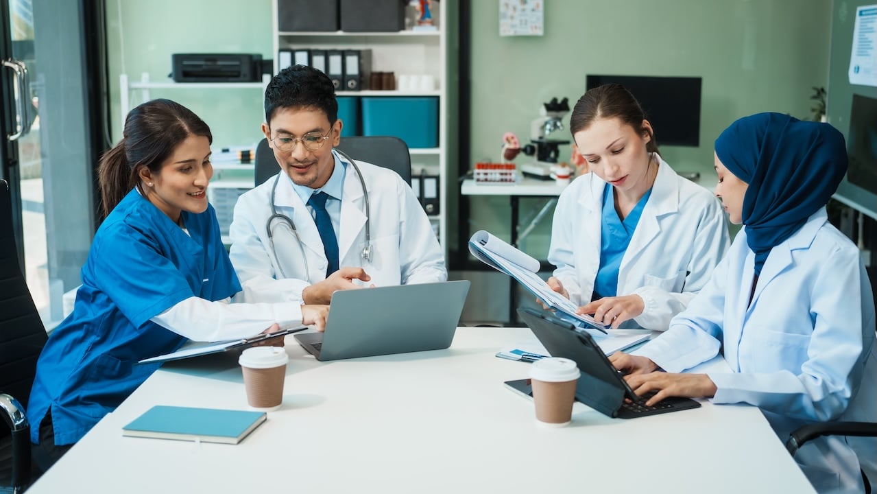 Healthcare professionals discussing patient information around a laptop and tablet in a clinical office