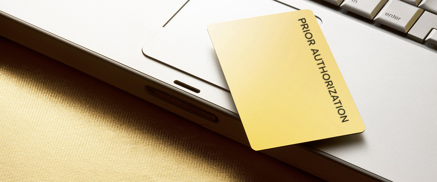 Gold card on top of laptop computer that says Prior Authorization