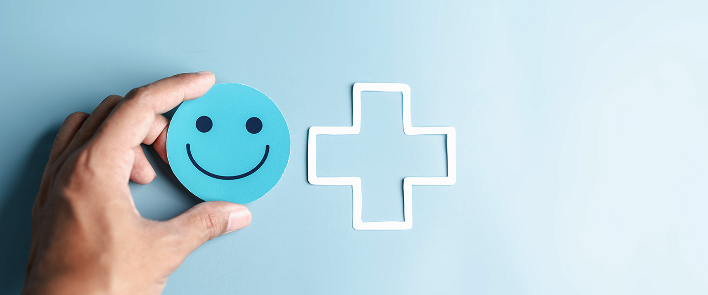 Image of person holding a smiley face with a health cross next to it on a blue background