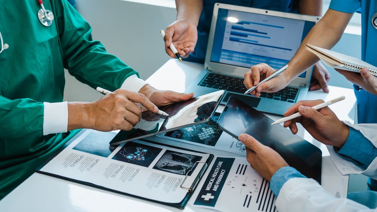 Medical team reviewing healthcare data on a tablet and laptop during a collaborative meeting